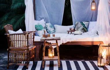 Cozy outdoor seating with bamboo furniture, striped rug, and hanging lanterns, surrounded by lush greenery.