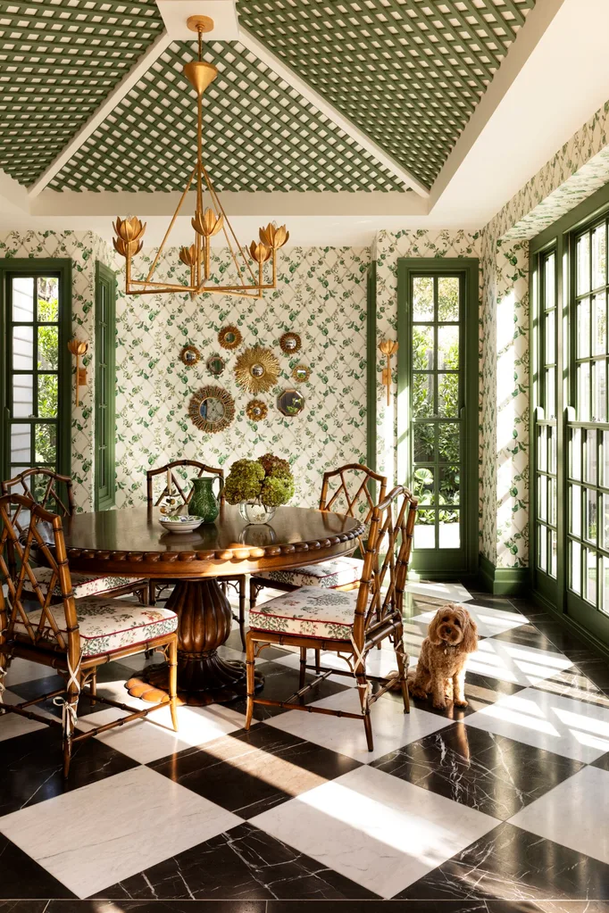 Elegant dining room with green lattice ceiling, floral wallpaper, round table, bamboo chairs, and a small dog on checkered floor