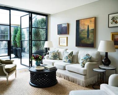 A living room with steel doors, landscape artworks and neutral furniture.