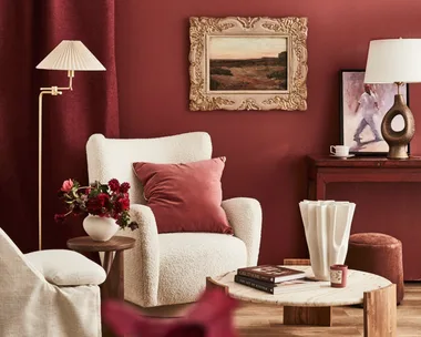 A red wall with a white armchair and a painting in a gilded frame