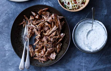 Shredded roast lamb in a bowl with two forks, beside a bowl of yogurt sauce and a bowl of salad.