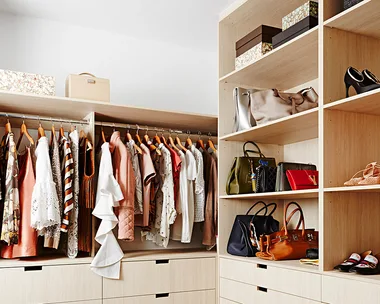Spacious walk-in closet with clothes on hangers, handbags, and shoes neatly arranged on shelves and drawers.