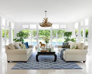 A modern country living room with white and blue furnishings overlooking the pool.