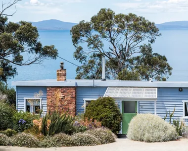 This fishing shack has been renovated into a colourful and pattern-filled Airbnb in Tasmania. The blue panelled exterior matches the blue of the sea views visible beyond the house.