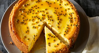 Passion fruit cheesecake with one slice cut, topped with passion fruit seeds, served on a grey plate.