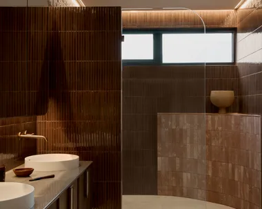 Modern bathroom with burgundy kit-kat tile walls, round basins in a marble vanity top, and a curved pink tiled half-height wall which softens a corner of the room.