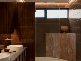Modern bathroom with burgundy kit-kat tile walls, round basins in a marble vanity top, and a curved pink tiled half-height wall which softens a corner of the room.