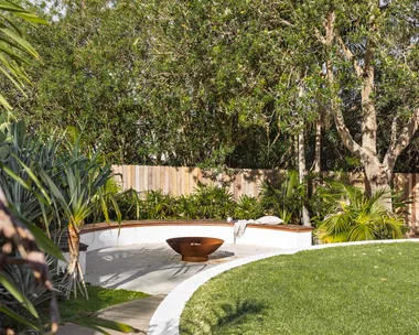 Coastal, tropical garden with curved wall, fence and lawn.