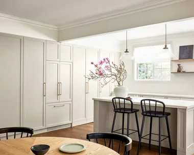 A modern neutral kitchen with shaker style cabinets, an island and timber table.