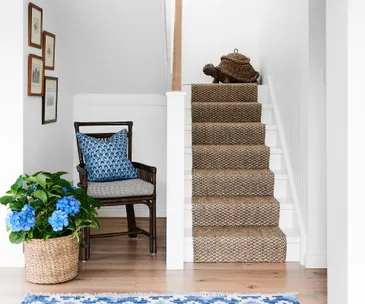Chair with blue cushion, basket of blue flowers, staircase with woven rug, and woven turtle decor on top step.