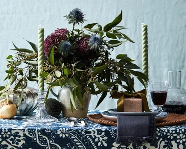 A blue tablecloth with a large vase of flowers on top and two spiral candlesticks