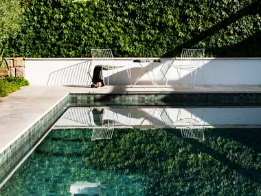 A rectangular swimming pool, surrounded by large stone pavers with a wall covered in Boston ivy in the background.