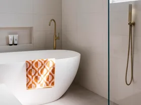 A bright, contmporary bathroom with a freestanding bath and orange patterned towel.
