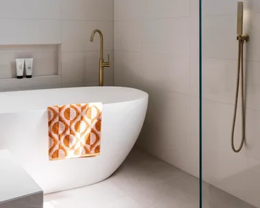 A bright, contmporary bathroom with a freestanding bath and orange patterned towel.
