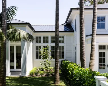 Large white house with palm trees and lush green lawn in sunny garden setting.