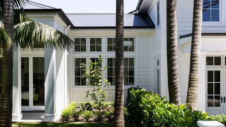 Large white house with palm trees and lush green lawn in sunny garden setting.