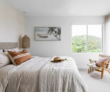 Modern bedroom with a neutral palette, large bed, window view of greenery, and tropical artwork on the wall.