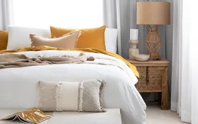 Bedroom setting with sheer curtains an upholstered bench seat at the base of the bed and butter yellow cushions on the bed