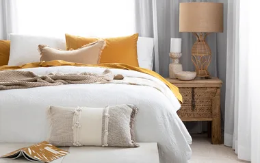 Bedroom setting with sheer curtains an upholstered bench seat at the base of the bed and butter yellow cushions on the bed