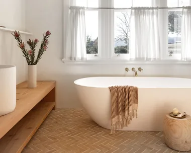 A modern country bathroom in white with terracotta tiles and a freestanding tub.