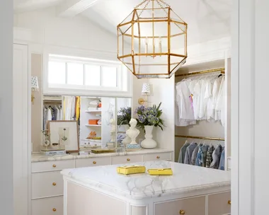 A white dressing room with a gold geometric pendant and marble drawers.