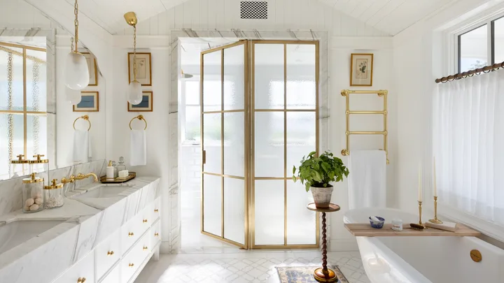 An all-white ensuite with gold glass doors, a freestanding bath and a marble vanity.