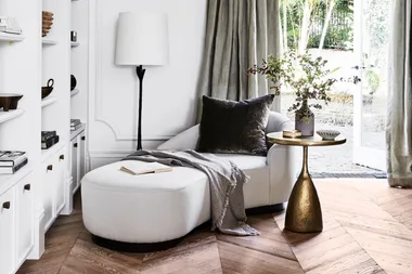 Elegant living room with a light grey couch, gold side table, and floor lamp by a window with soft curtains.