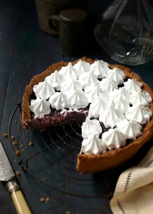 Berry pie with whipped topping, one slice missing, on a dark wooden table with a knife and napkin nearby.