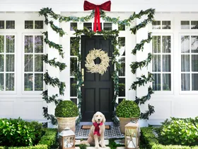White home exterior with white berry Christmas wreath on the front door and eucalyptus garlands wrapped around portico collumns