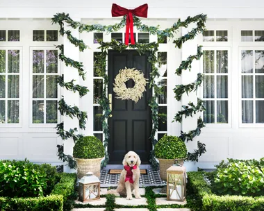 White home exterior with white berry Christmas wreath on the front door and eucalyptus garlands wrapped around portico collumns