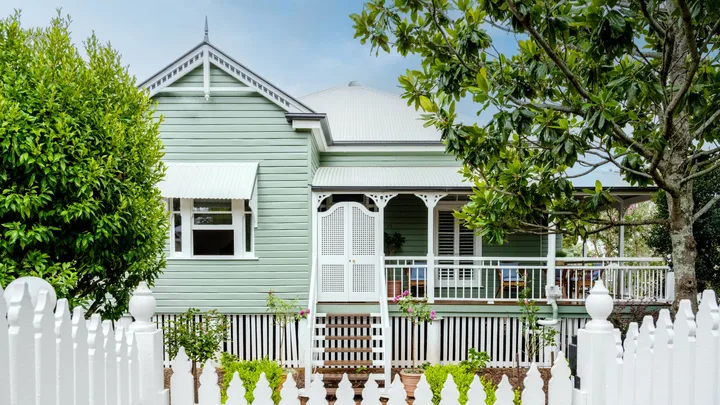 A traditional Queensland cottage with green cladding and white fretwork.