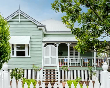 A traditional Queensland cottage with green cladding and white fretwork.