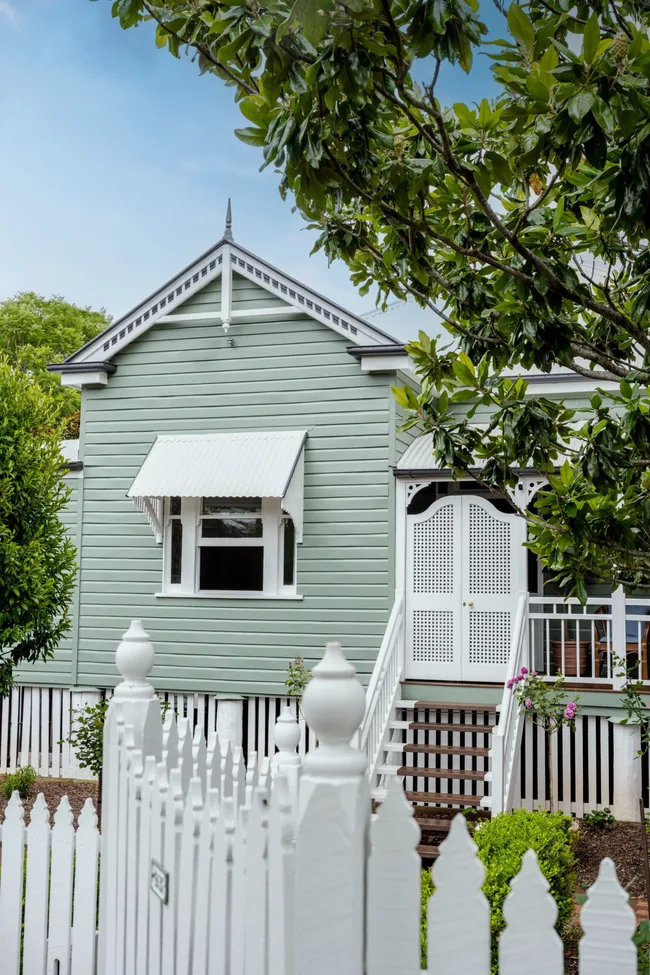 A classic Queenslander cottage with green cladding and white window detailing.