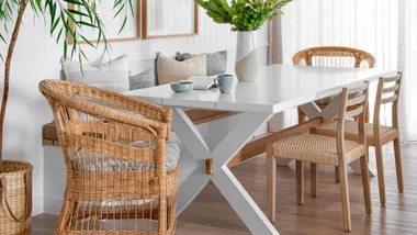 Bright dining area with a white table, wicker chairs, and green plant decor.