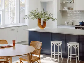 A contemporary kitchen with a blue island, rounded pendants and a timber table.