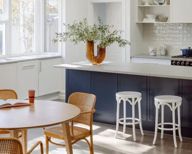 A contemporary kitchen with a blue island, rounded pendants and a timber table.