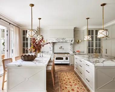 A large classic-style kitchen with two marble islands, a freestanding cooker and hanging lights.