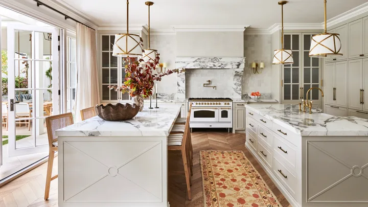 A large classic-style kitchen with two marble islands, a freestanding cooker and hanging lights.