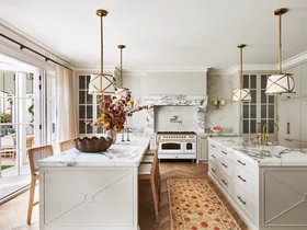 A large classic-style kitchen with two marble islands, a freestanding cooker and hanging lights.