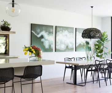 Bright dining room with modern decor, featuring a table, chairs, abstract art, pendant light, and plants.