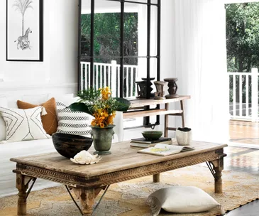 Cozy living room with wooden coffee table, decorative pillows on sofa, and a large window overlooking greenery.
