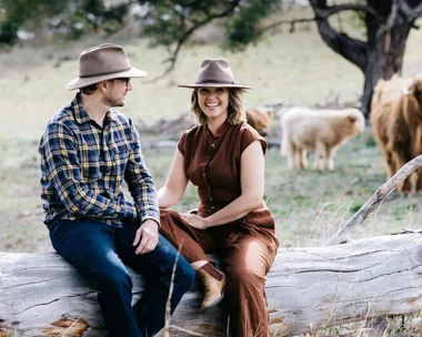 Edwina Bartholomew and Neil Varcoe on a log with pet cows in the background.