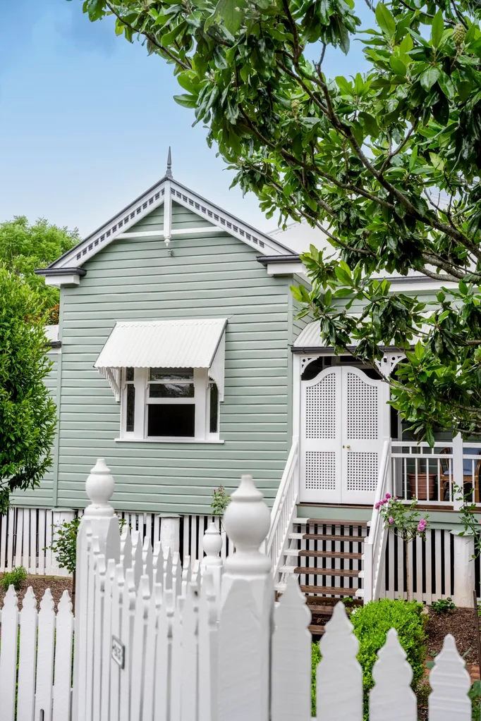 This classic Queenslander cottage has the trending exterior paint colour of Dulux Remote Control, a relaxing sage green, beside white trims and a white picket fence.