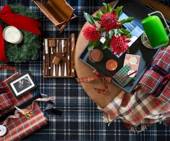 Birds-eye view of an ottoman and tartan rug styled like a tablescape with festive decor, gifts and homewares.