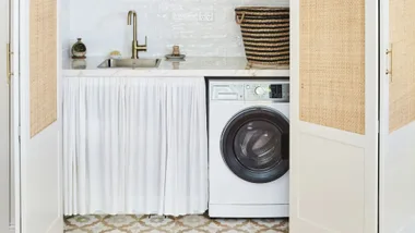 Laundry room with white washer, sink, woven basket, and patterned tile floor.