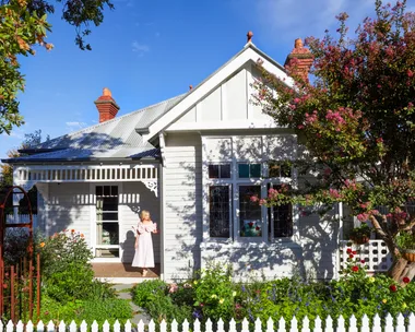 Fleur Harris stands on the deck of her heritage home, which has a thriving cottage garden out the front and a white picket fence.