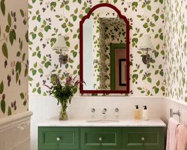 A green bathroom with botanical wallpaper, white tiled wainscoting and green bathroom joinery.