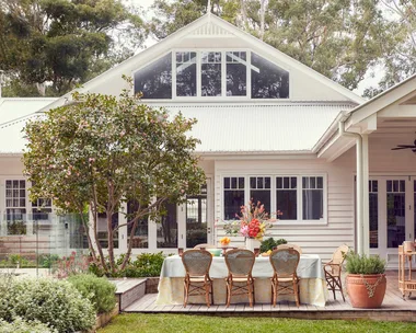 An exterior photo of a white house with an outdoor dining area with rattan styling