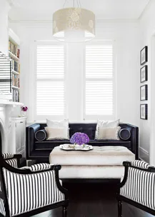 Elegant living room with black sofa, striped chairs, and a ceiling light. Purple flowers in a vase on the coffee table.