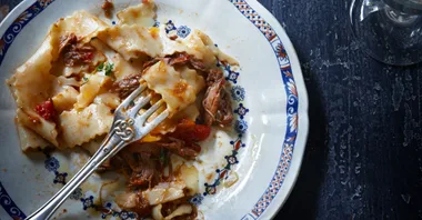 Plate of pasta with slow-cooked meat, tomato sauce, and a fork, on a white and blue decorative plate.
